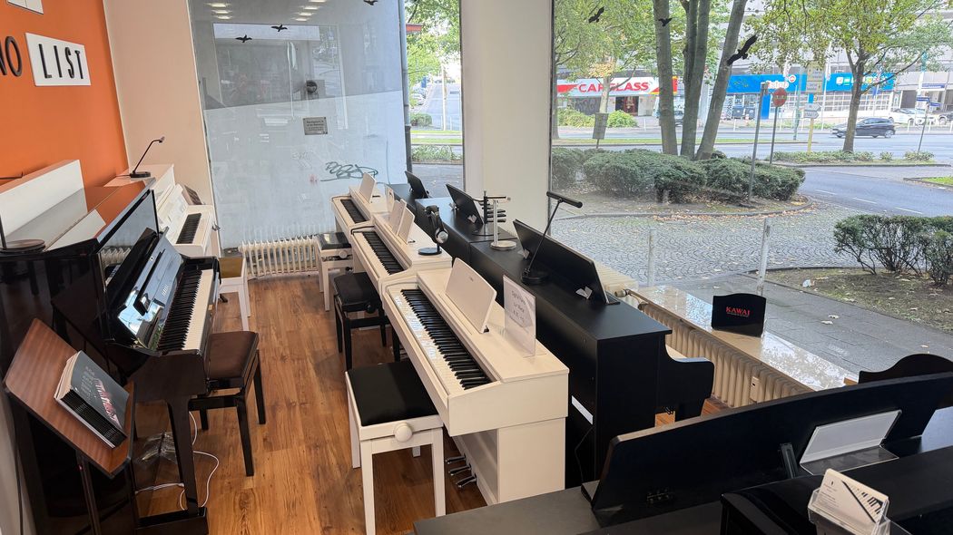 Moderne Musikschule mit mehreren Klavieren und Sitzgelegenheiten, Blick ins Freie.